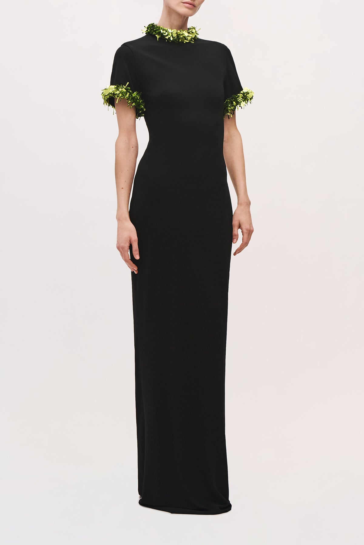 Front view of a model wearing the Bex Gown in Black/Green Glo, a fitted floor-length gown with short sleeves and green sequin trim at the neckline and cuffs.