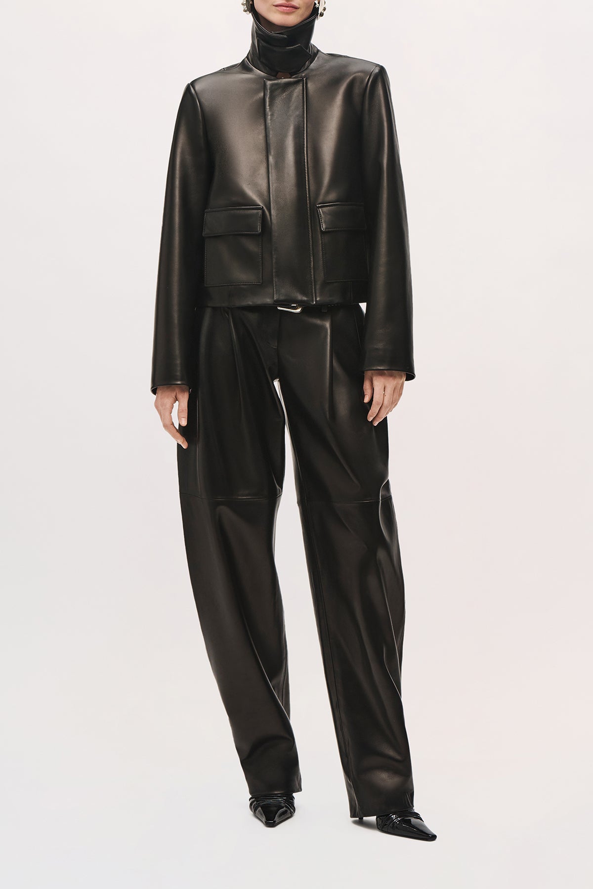 Front product view of a model wearing the Remi Jacket in black with a popped pointed collar, two pockets, and a cropped fit.