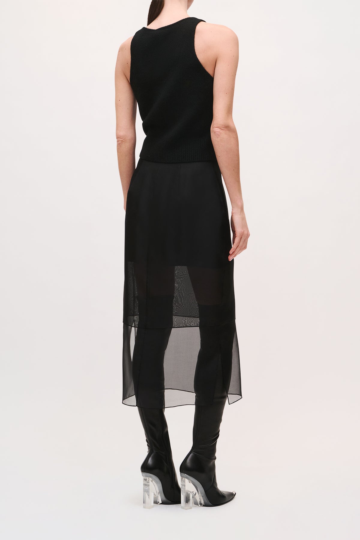 Back view of model wearing the Brett Skirt in Black with a fitted midi skirt with sheer lower panels and an asymmetrical hem.
