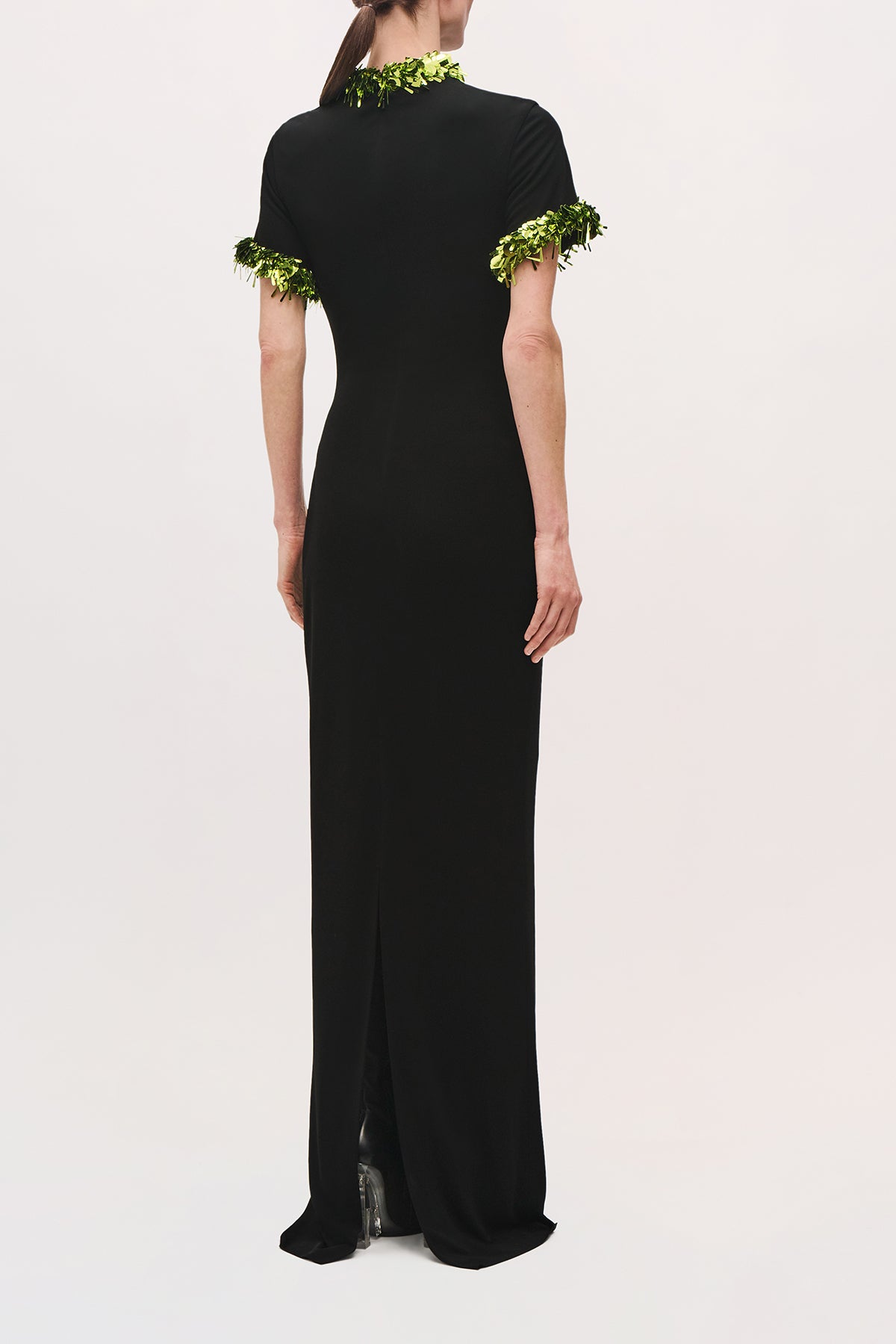 Back view of a model wearing the Bex Gown in Black/Green Glo, featuring a fitted shape and green sequin trim at the neckline and cuffs.