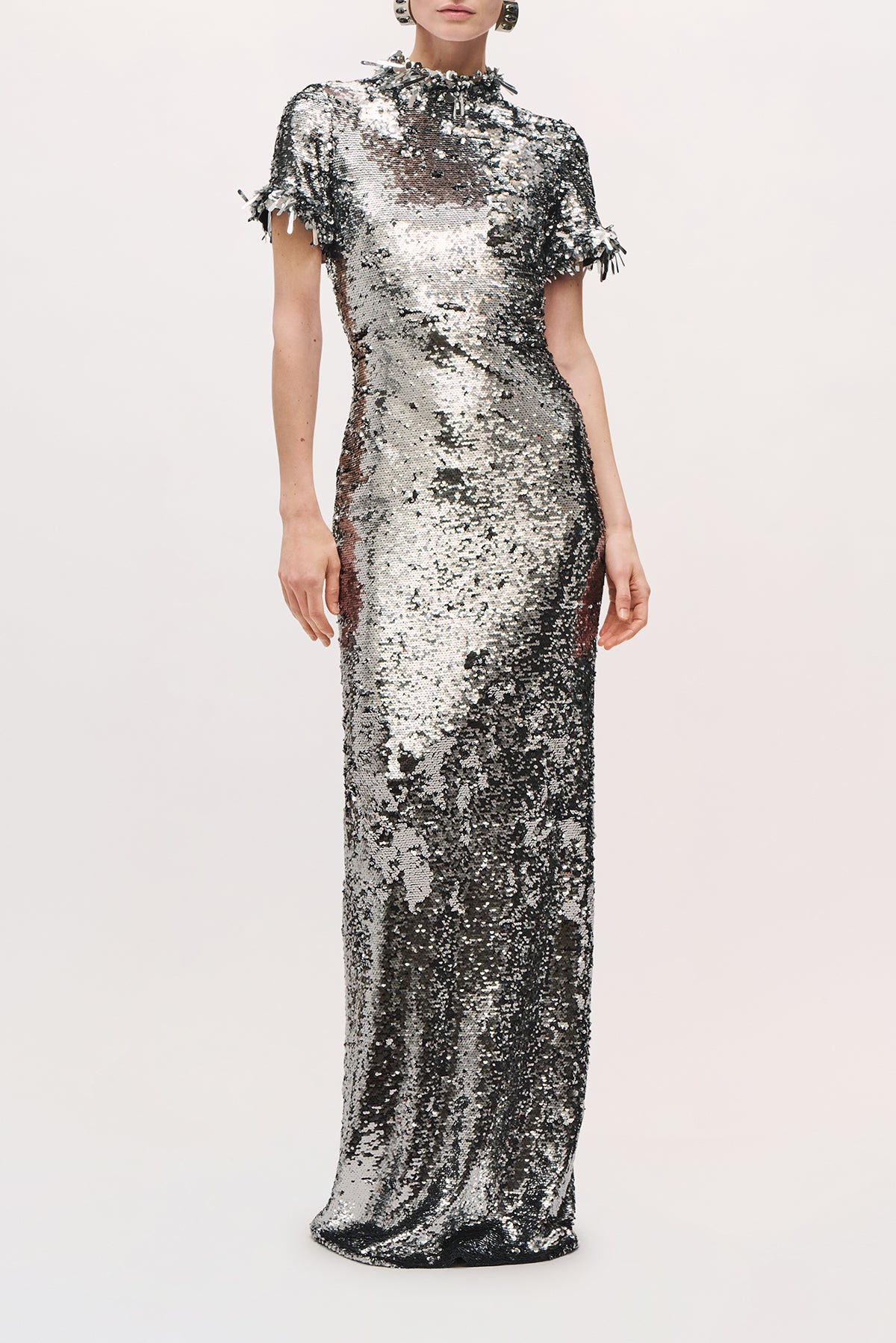 Front view of a model wearing the Bex Gown in Silver, a fitted floor-length sequin gown with short sleeves. 