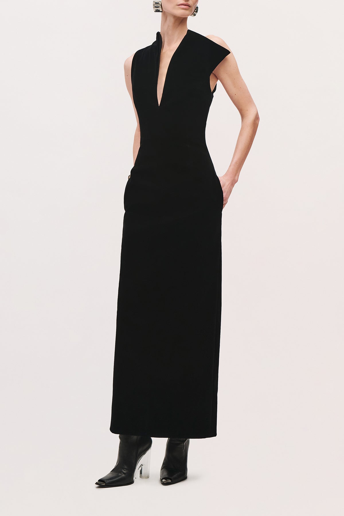 Front view of a model with a hand in pocket wearing the Farren Dress in Black, a sleeveless long dress with a deep V-neckline and straight silhouette.