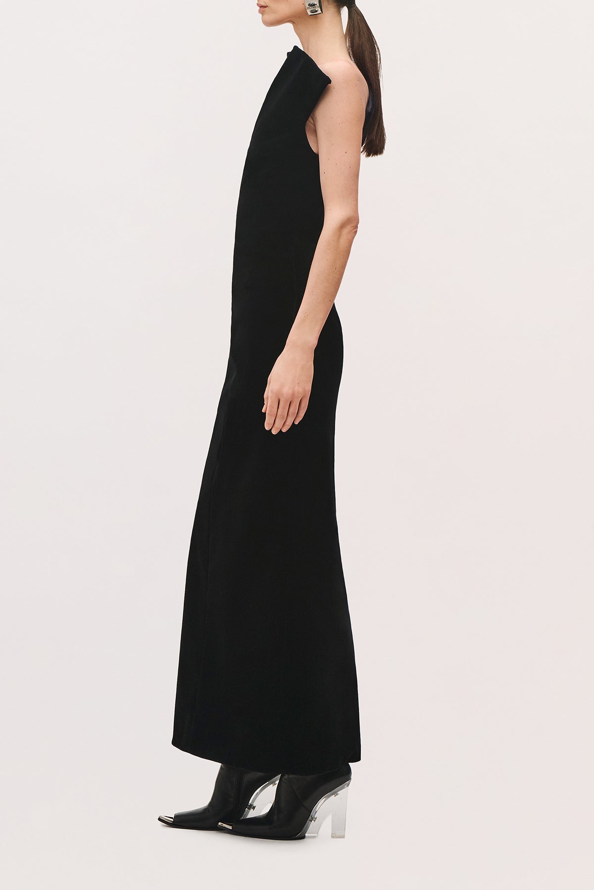 Side view of a model wearing the Farren Dress in Black, showing its straight silhouette, long length, and one shoulder detail.