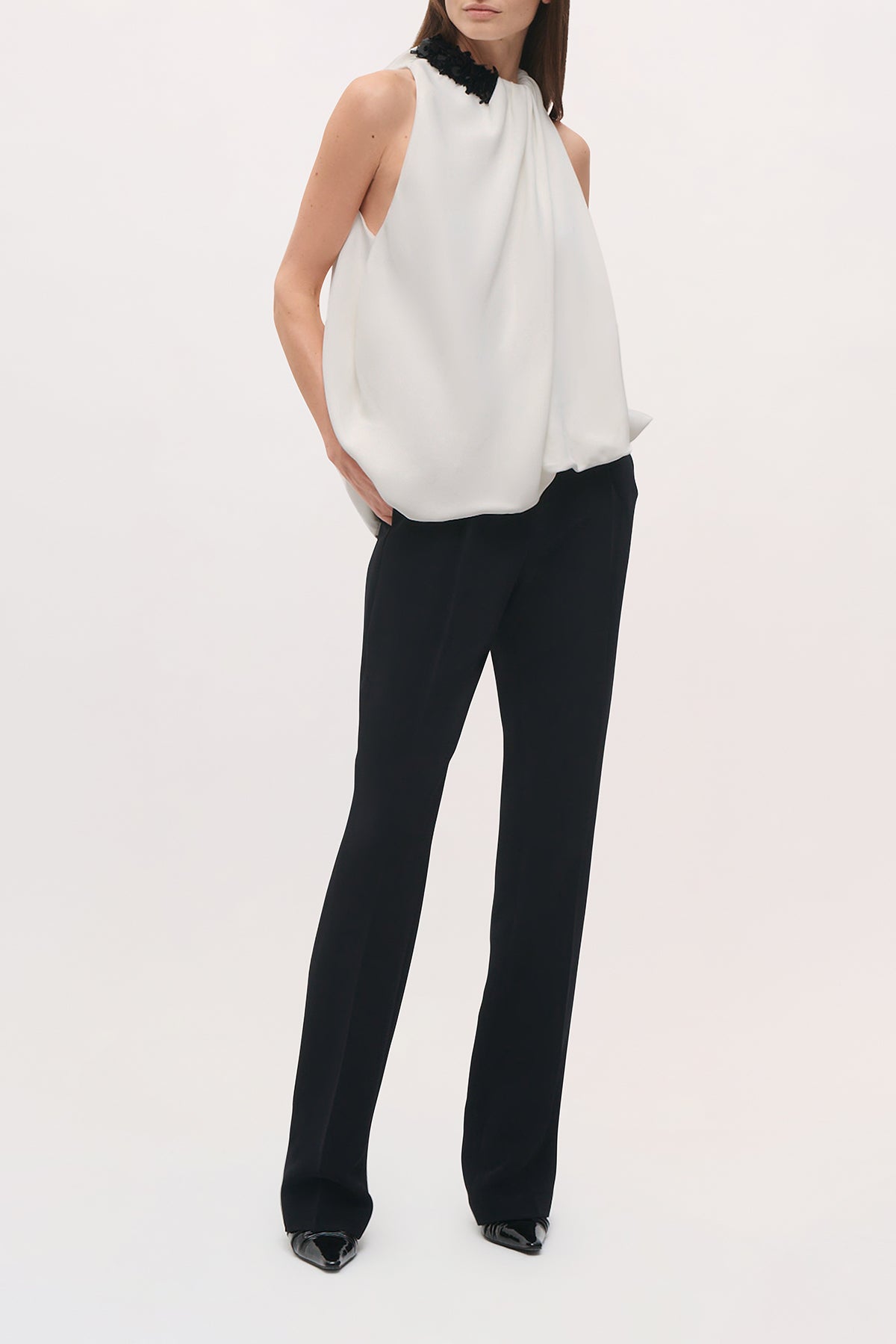 Angled front view of a model wearing the Haze Top in Ivory/Black, featuring a loose sleeveless silhouette, gathered neckline, black sequin shoulder detail, and softly draped asymmetric hem.