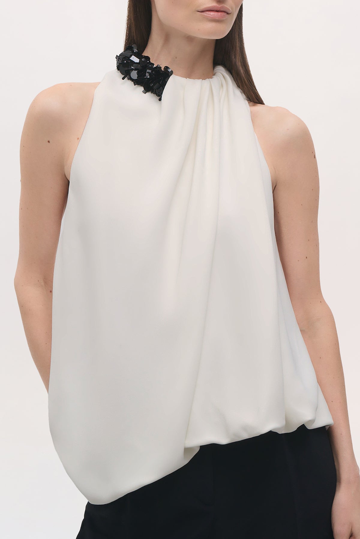 Cropped front view of a model wearing the Haze Top in Ivory/Black, showing its high gathered neckline, draped front and black sequin shoulder embellishment. 