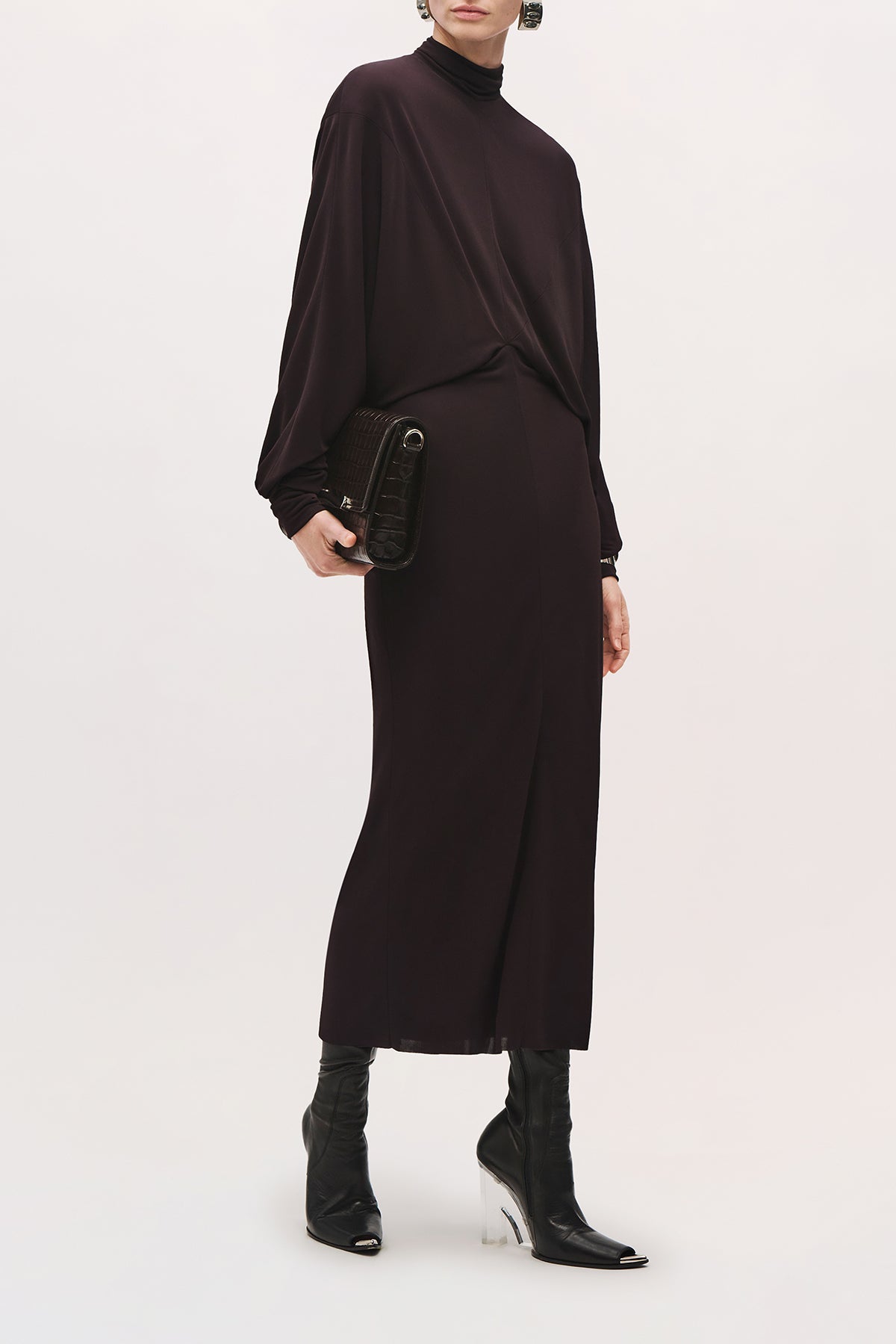 Front angled view of a model wearing the Helena Dress in Ganache, a long-sleeve midi dress with a draped bodice and fitted skirt. 