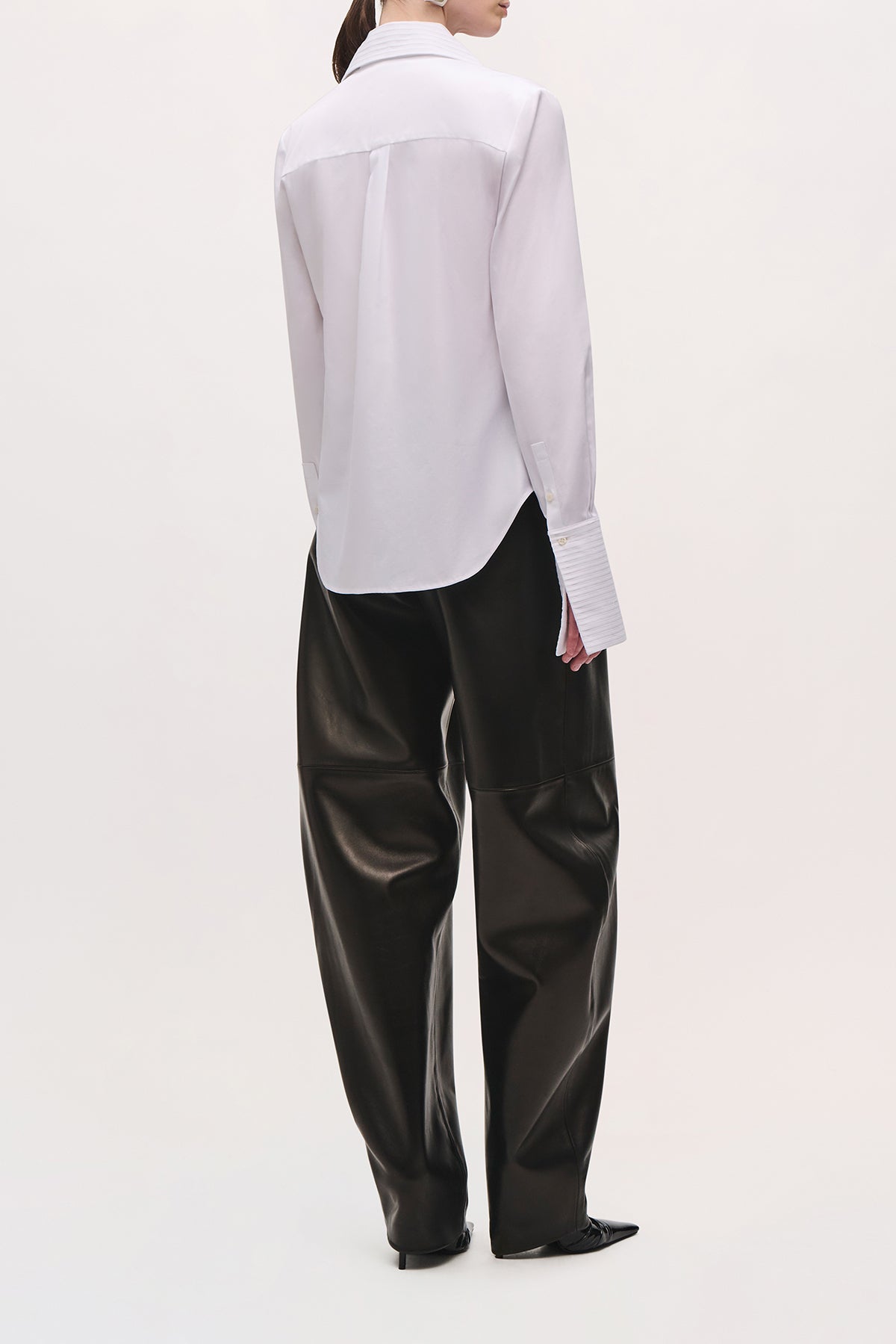 Back angled view of a model wearing the Inez Shirt in White with textured cuffs and long angled bodice. 