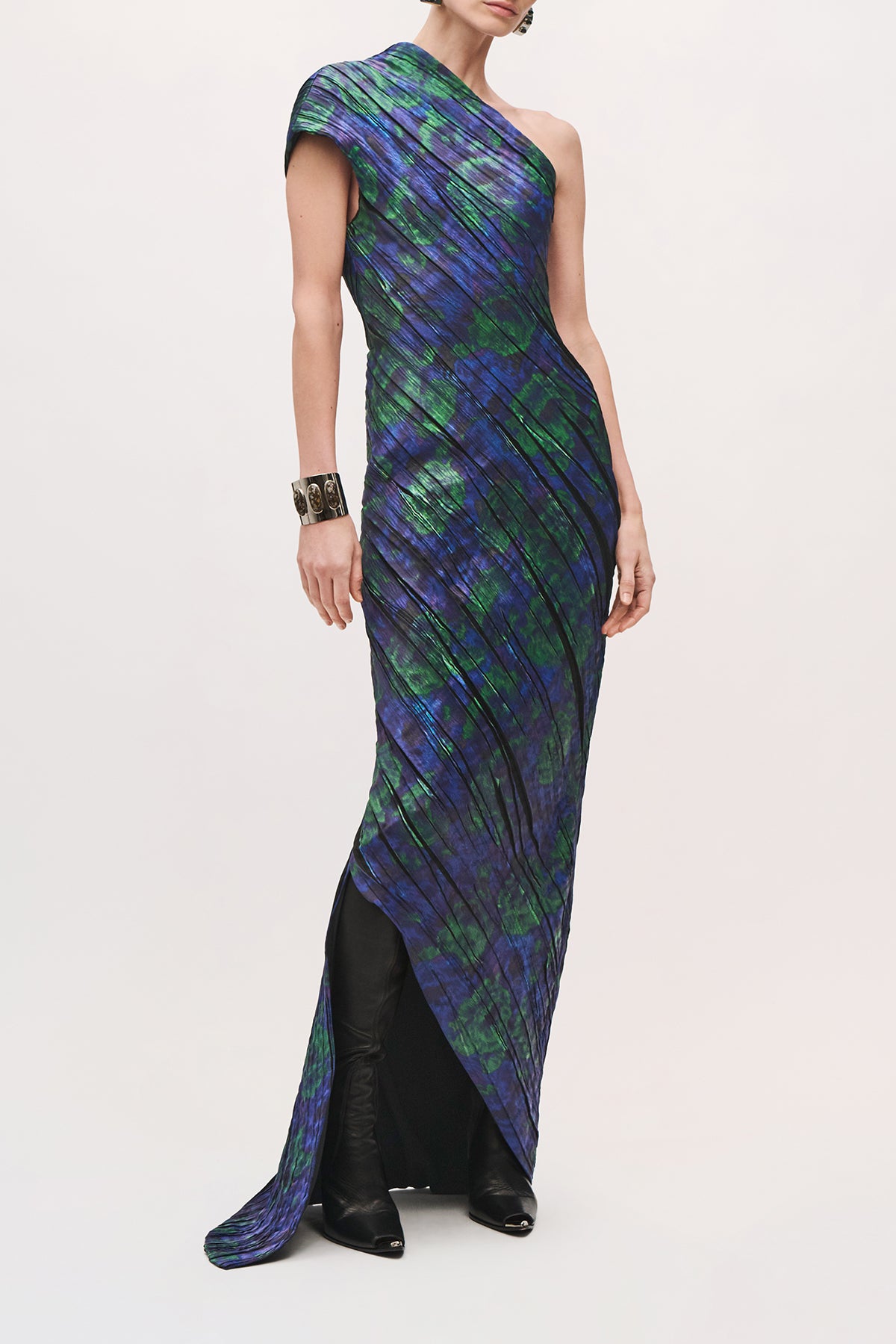 Front product view of a model wearing the Karina Dress in Blue Floral, with diagonal pleats throughout the dress, one shoulder, and asymmetric floor-length skirt.