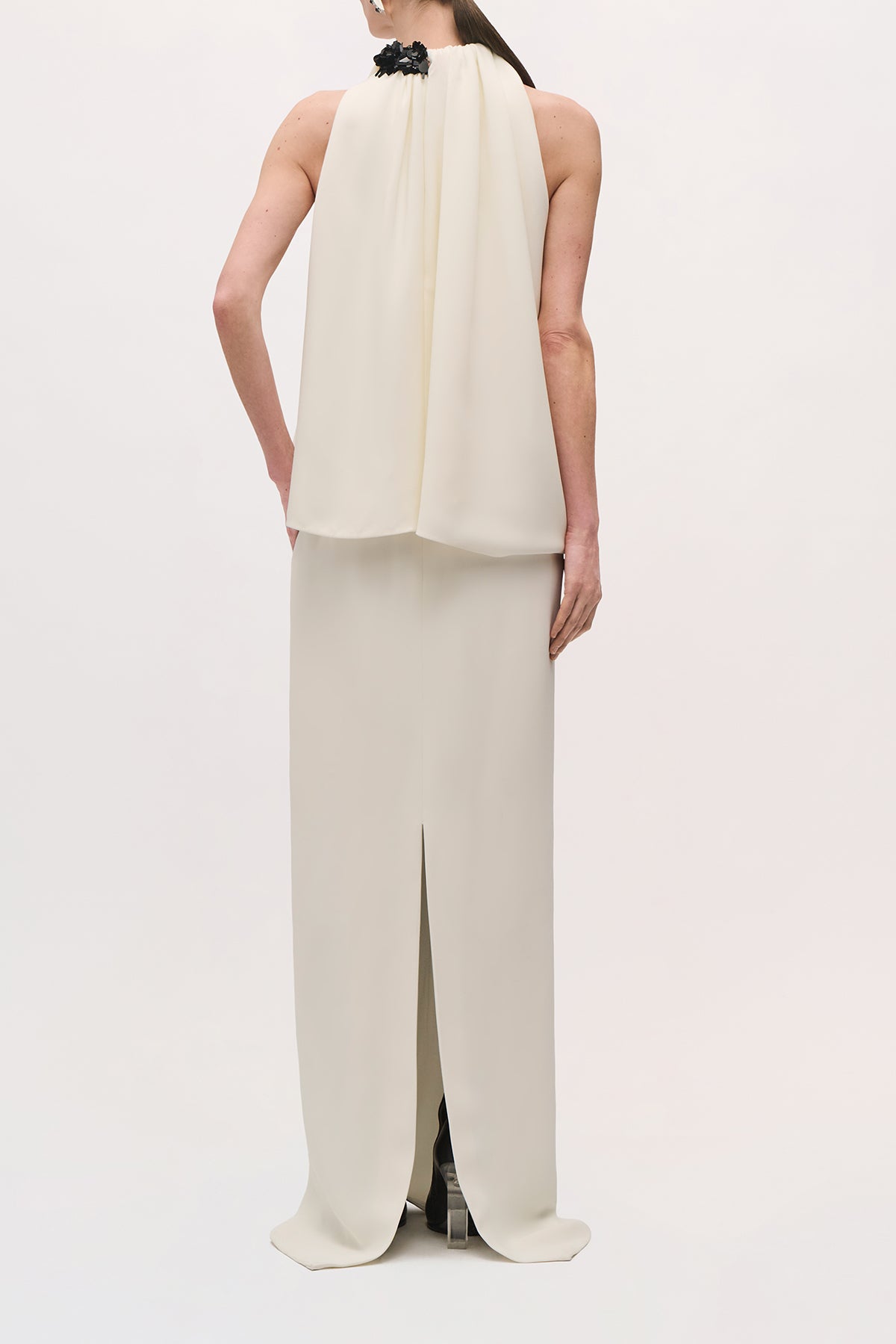 Back view of a model wearing the Petra Gown in Ivory;Black, featuring a flowing back bodice and center-back skirt slit. 