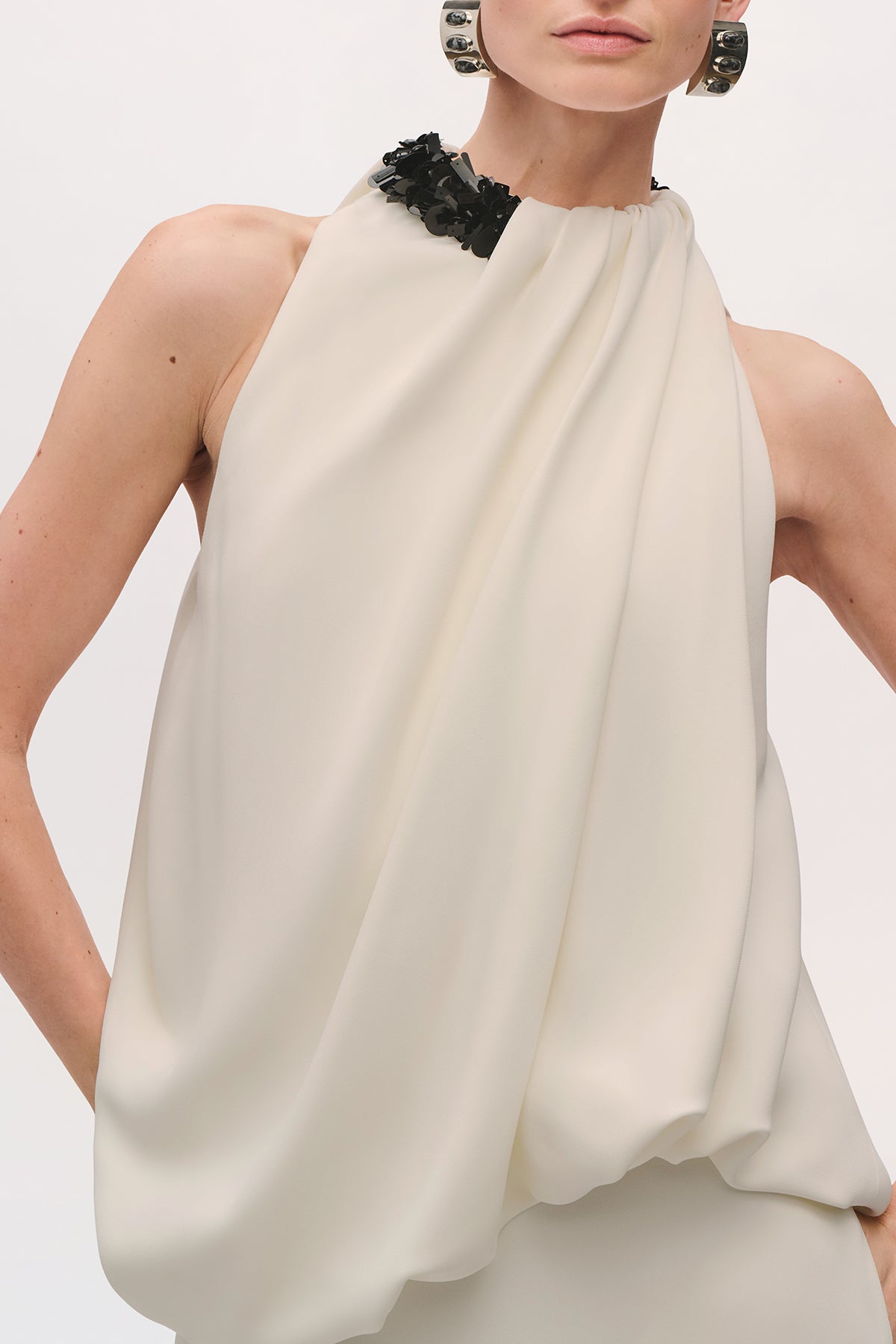 Close-up front view of a model wearing the Petra Gown in Ivory;Black, highlighting the gathered halter neckline and softly draped bodice.