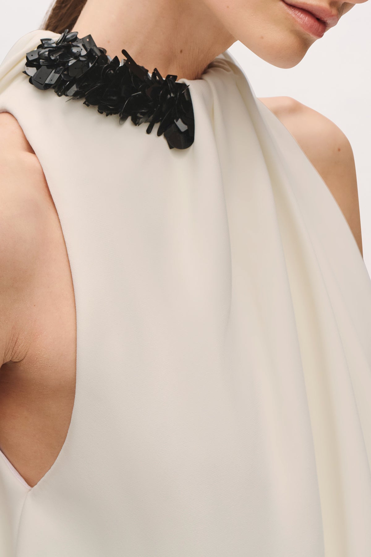 Detail shot of a model wearing the Petra Gown in Ivory;Black, highlighting the black embellished neckline and gathered ivory fabric.
