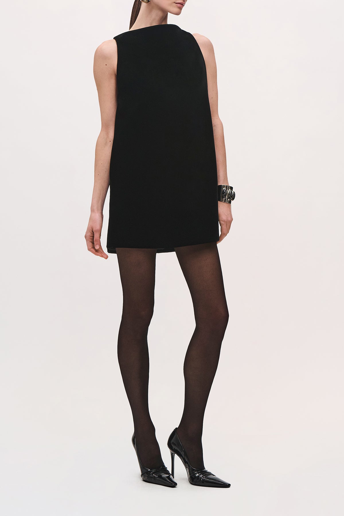 Front view of a model wearing the Sable Mini Dress in Black, with a structured straight silhouette and a draped mantle detail extending across the back.