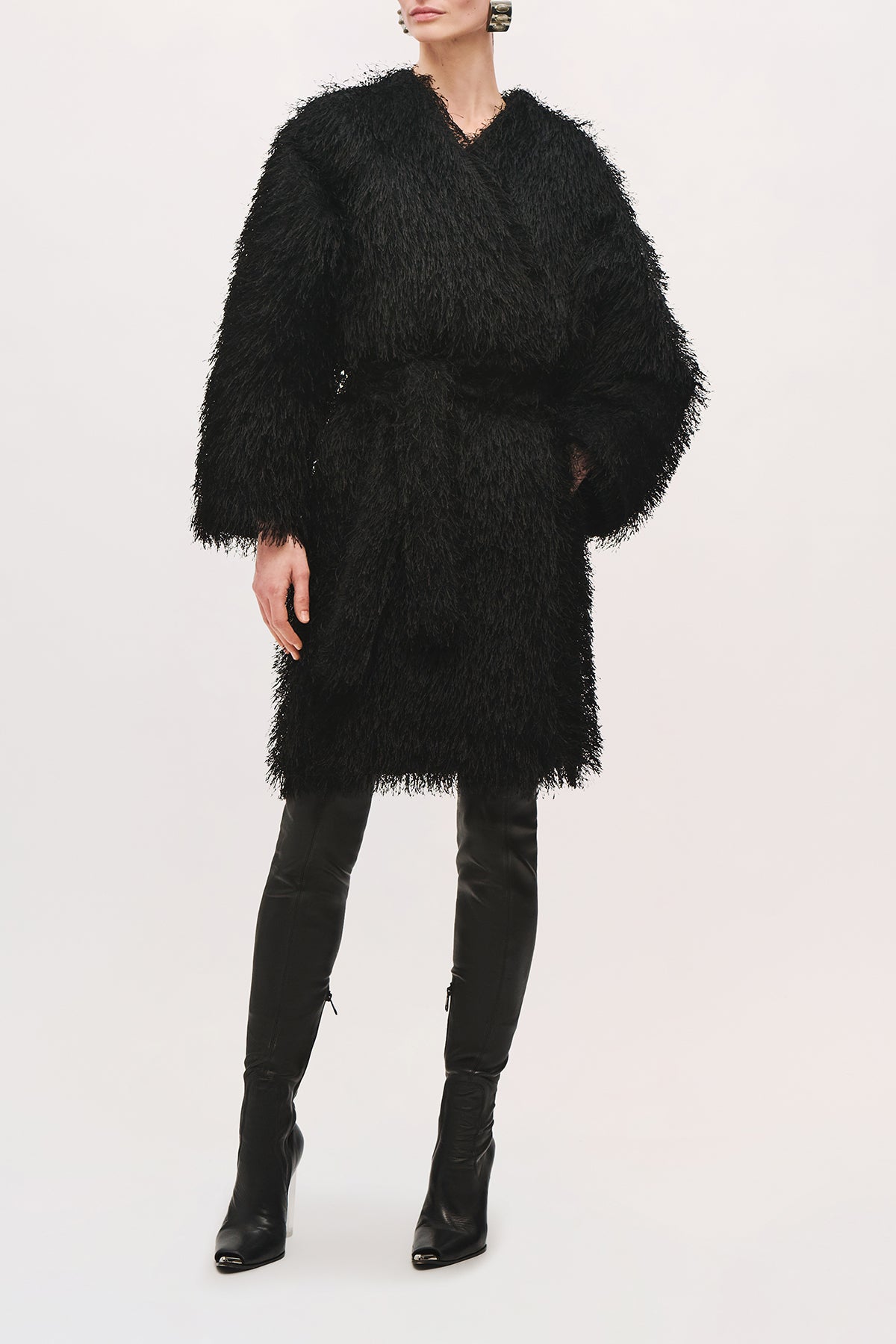 Front view of a model wearing the Sabrina Coat in Black, featuring a textured fringe finish, wrap-style front, wide long sleeves, self-tie belt, and knee-length silhouette.