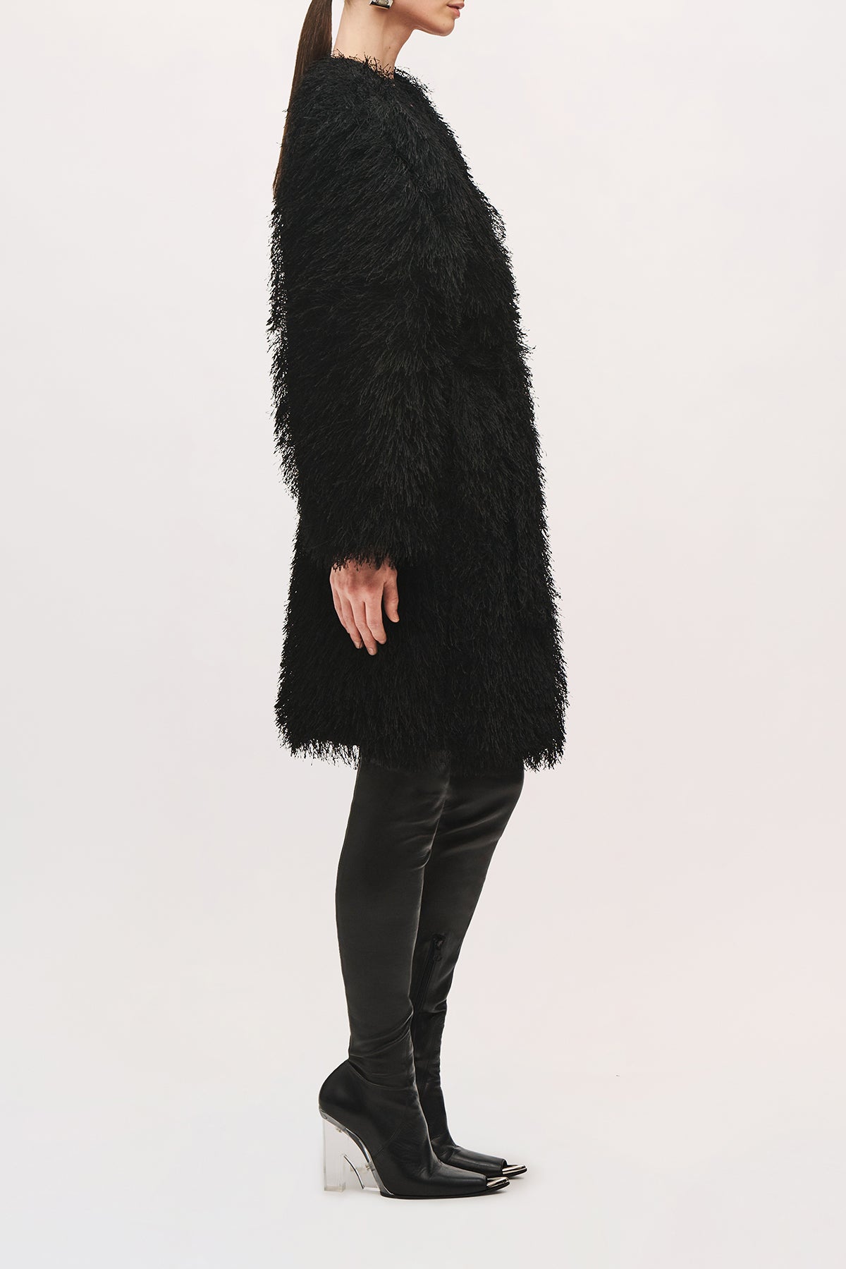 Side view of a model wearing the Sabrina Coat in Black, highlighting the oversized cocoon shape, textured fringe finish, wide sleeves, and straight knee-length hem.